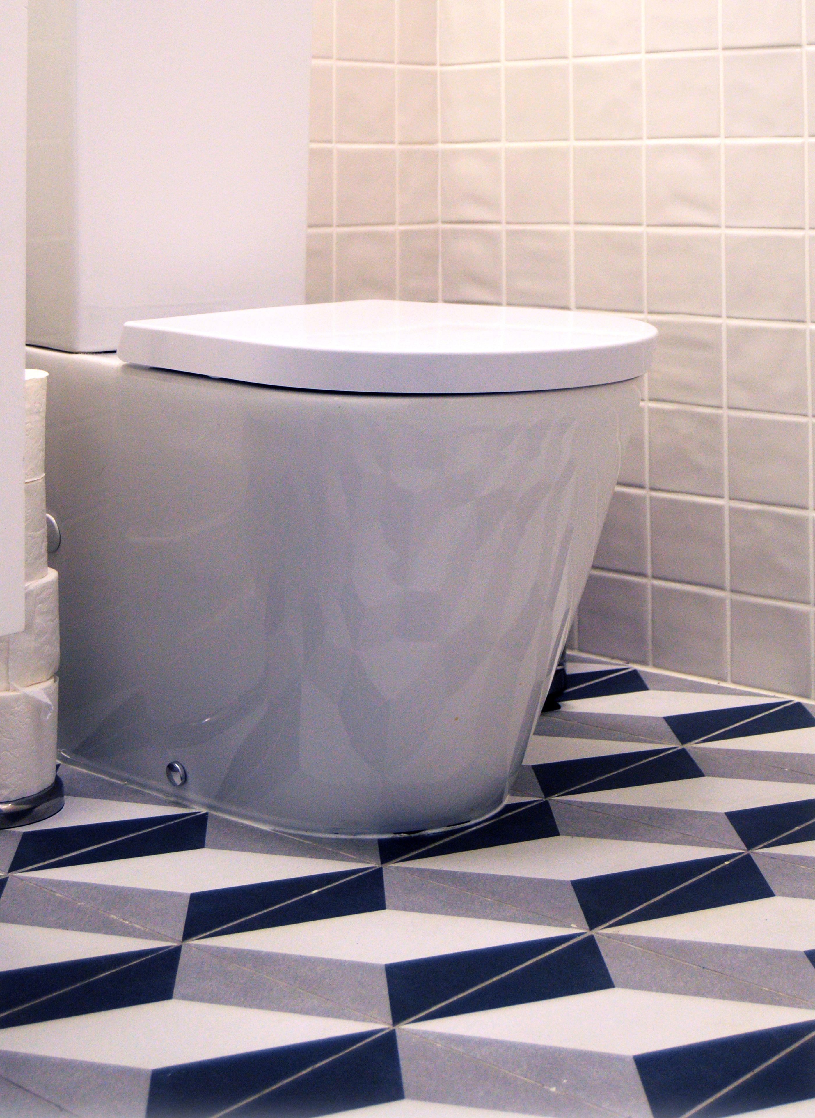 A toilet with a white lid, a toilet paper holder, and a patterned floor.