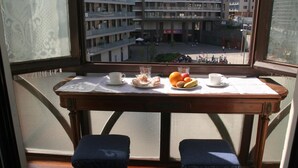Un balcón con una mesa dispuesta para el desayuno, con vistas a un paisaje urbano con varios edificios y una calle abajo.