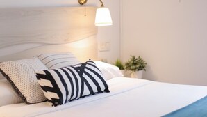 Una cama bien hecha con ropa blanca y dos almohadas, una a rayas y otra con estampado de lunares.