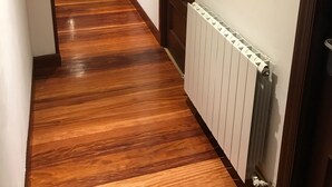 Un pasillo con suelo de madera, un radiador y una puerta con paneles de vidrio.