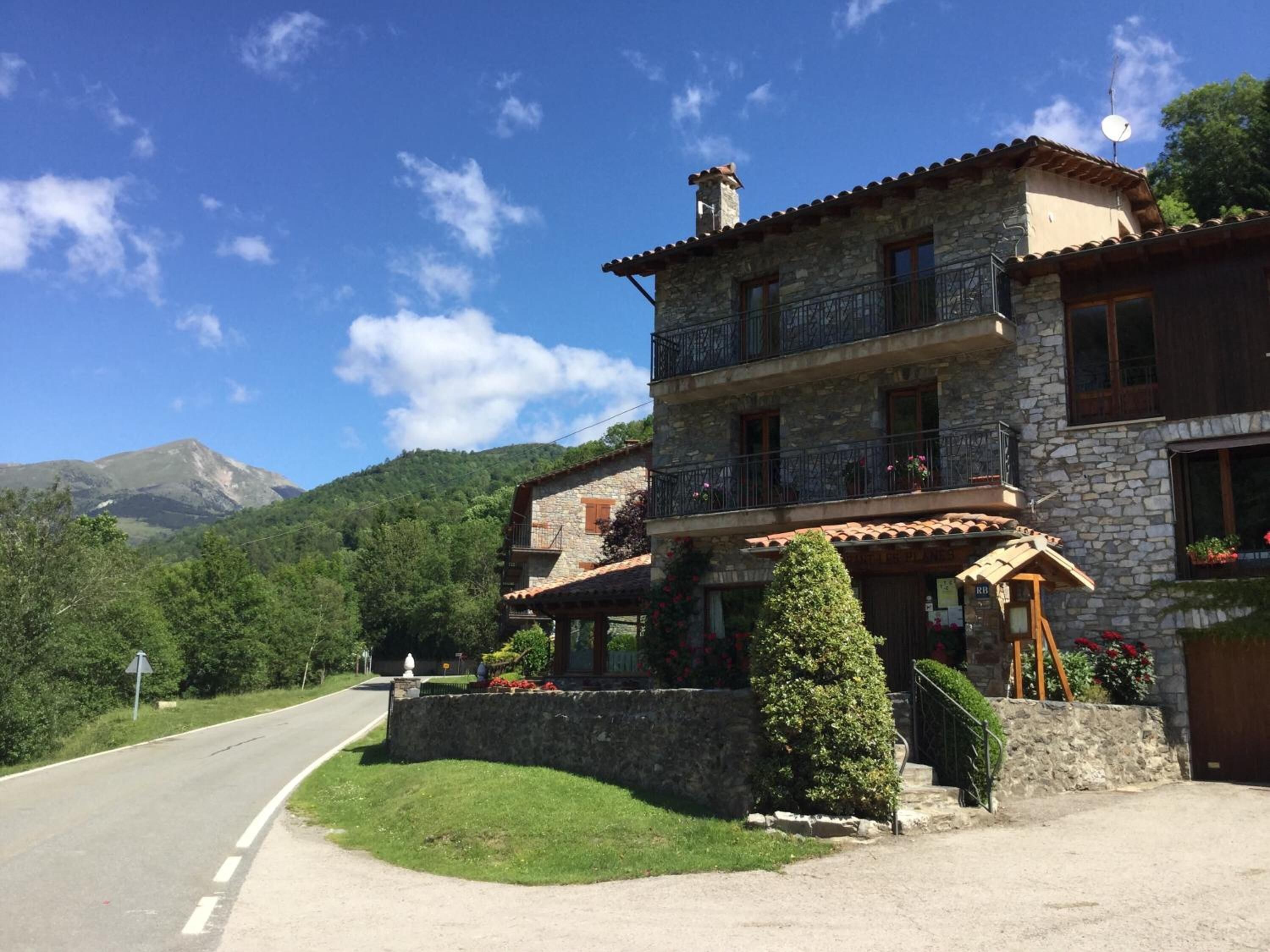 Un bâtiment en pierre de deux étages, doté de balcons et d’un escalier en pierre, avec une chaîne de montagnes en arrière-plan.