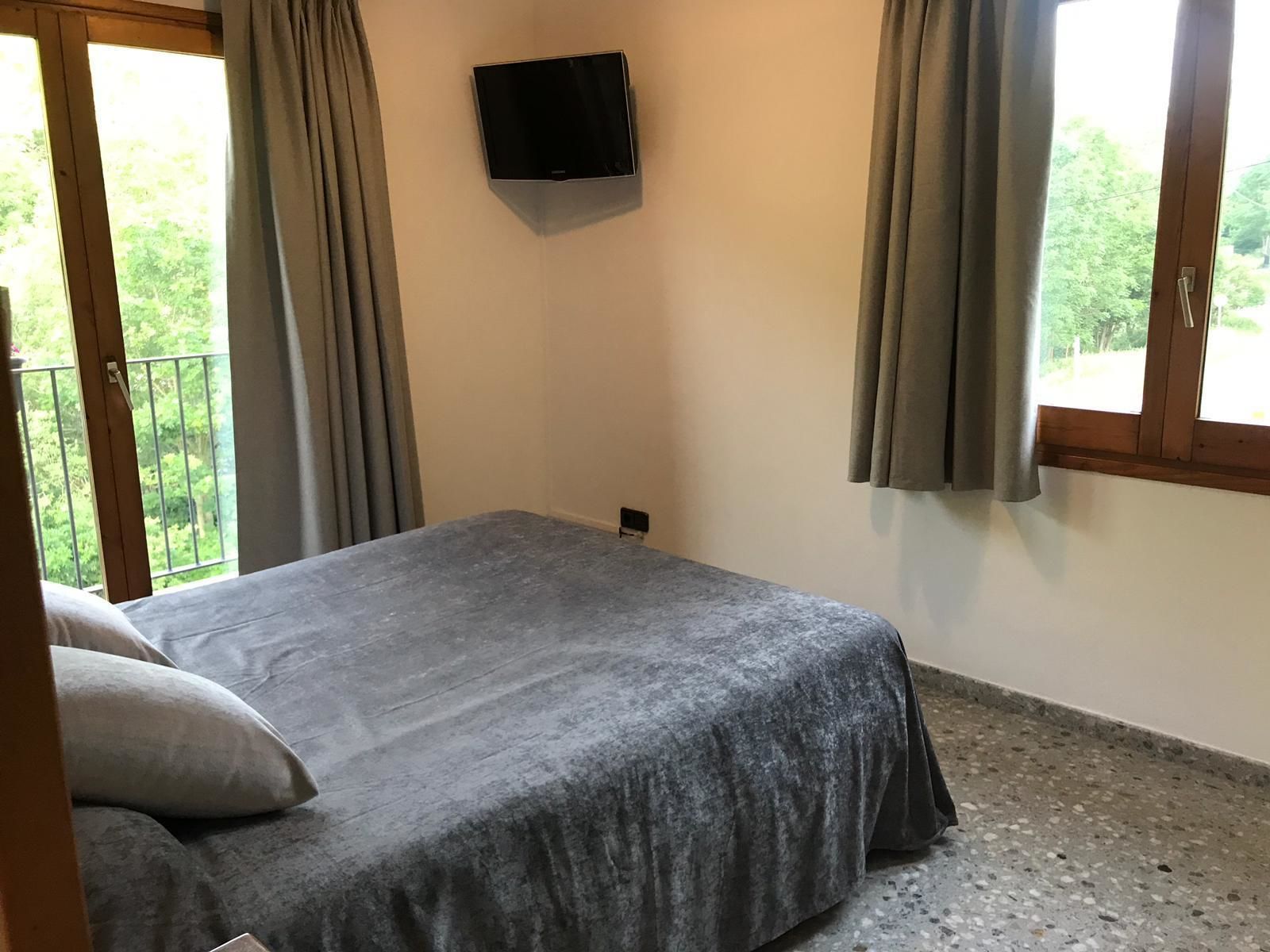 Une chambre à coucher avec un lit, un téléviseur fixé au mur et un balcon avec des rideaux.