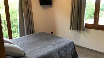 A bedroom with a bed, a TV mounted on the wall, and a balcony with curtains.