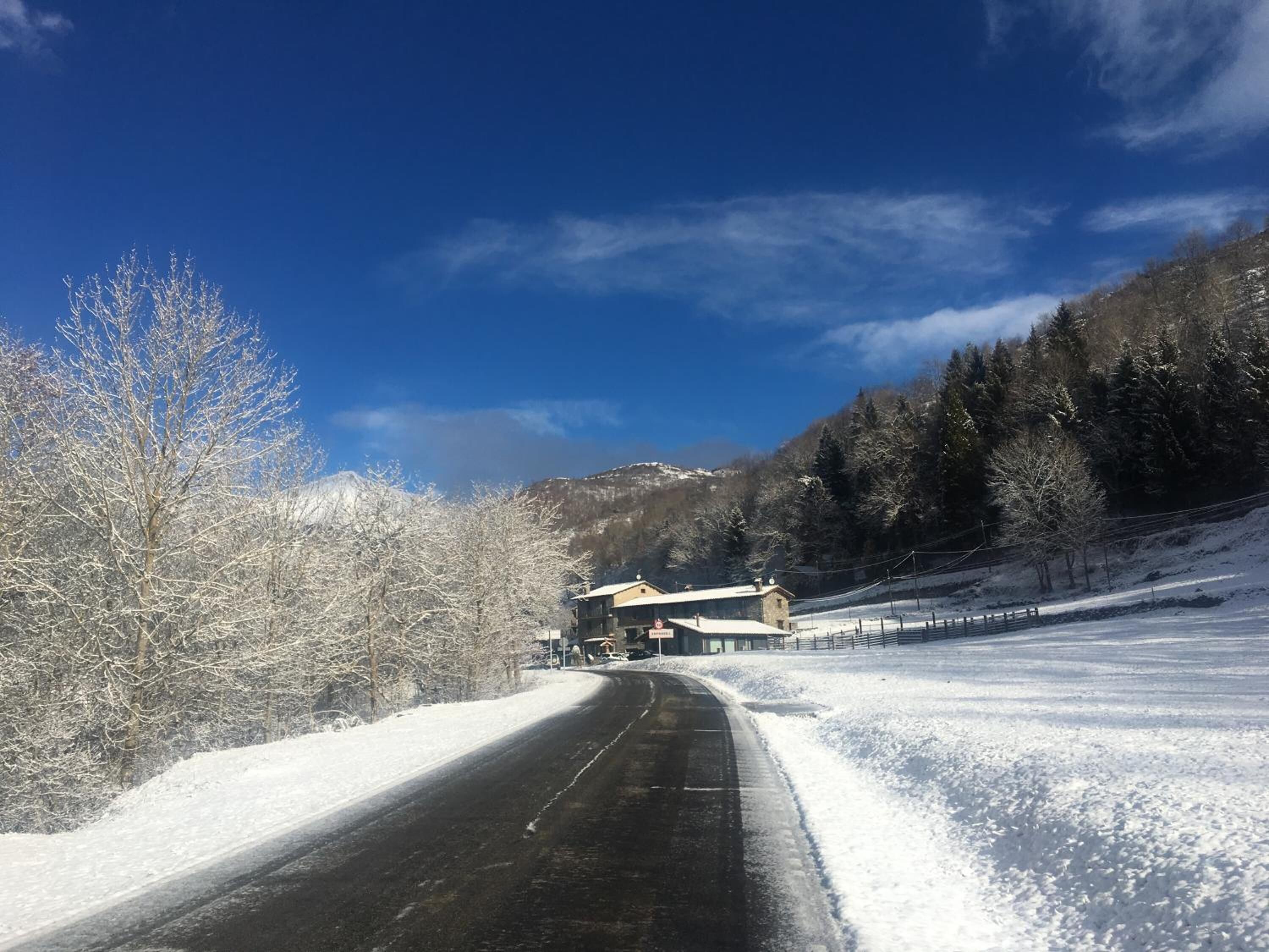 Una carretera cubierta de nieve con un edificio a la derecha, rodeada de árboles y montañas.