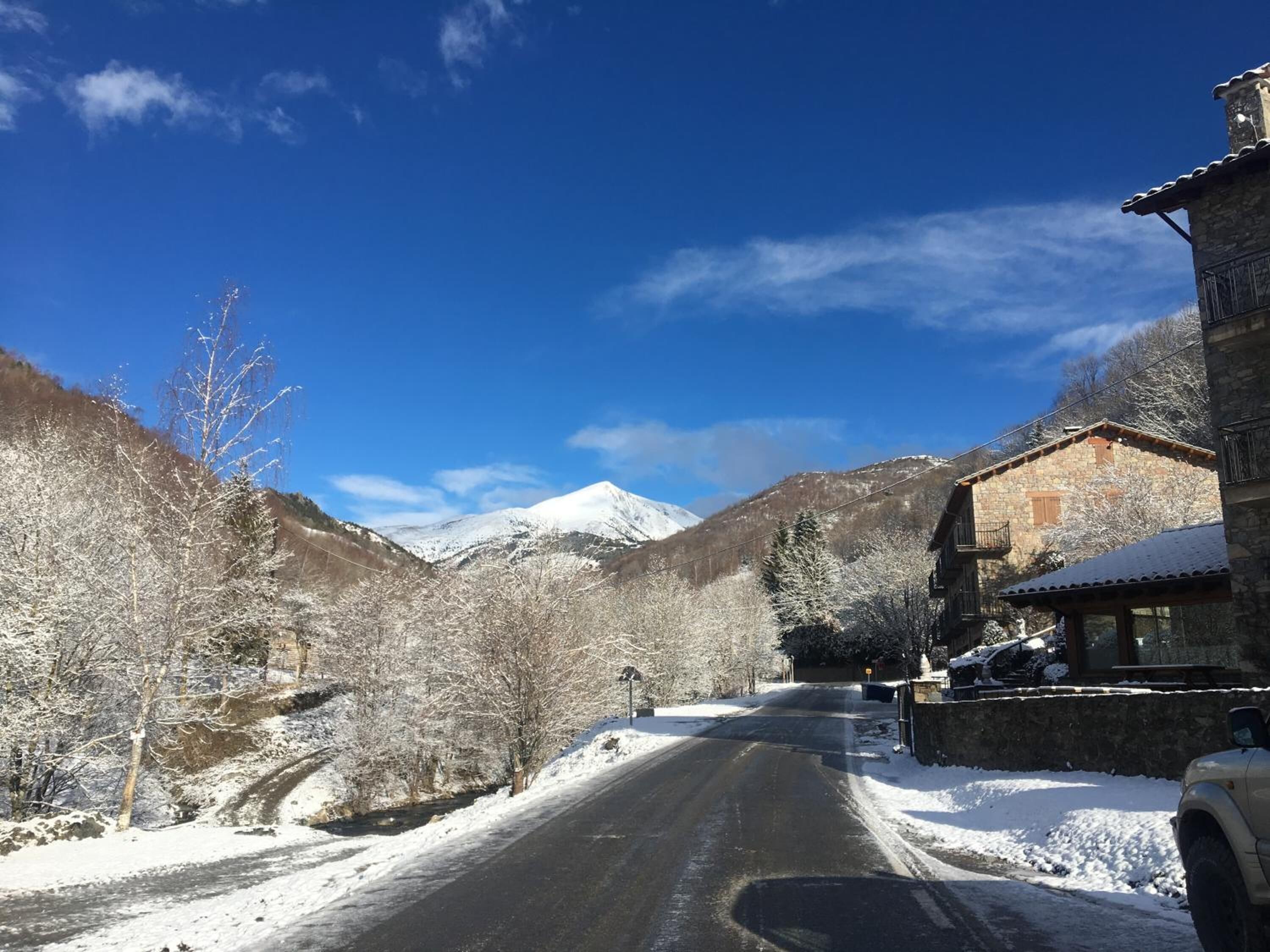 Une route de montagne enneigée, avec un bâtiment en pierre sur la droite.