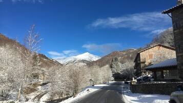 Una carretera nevada que serpentea por la montaña, con un edificio de piedra a la derecha.