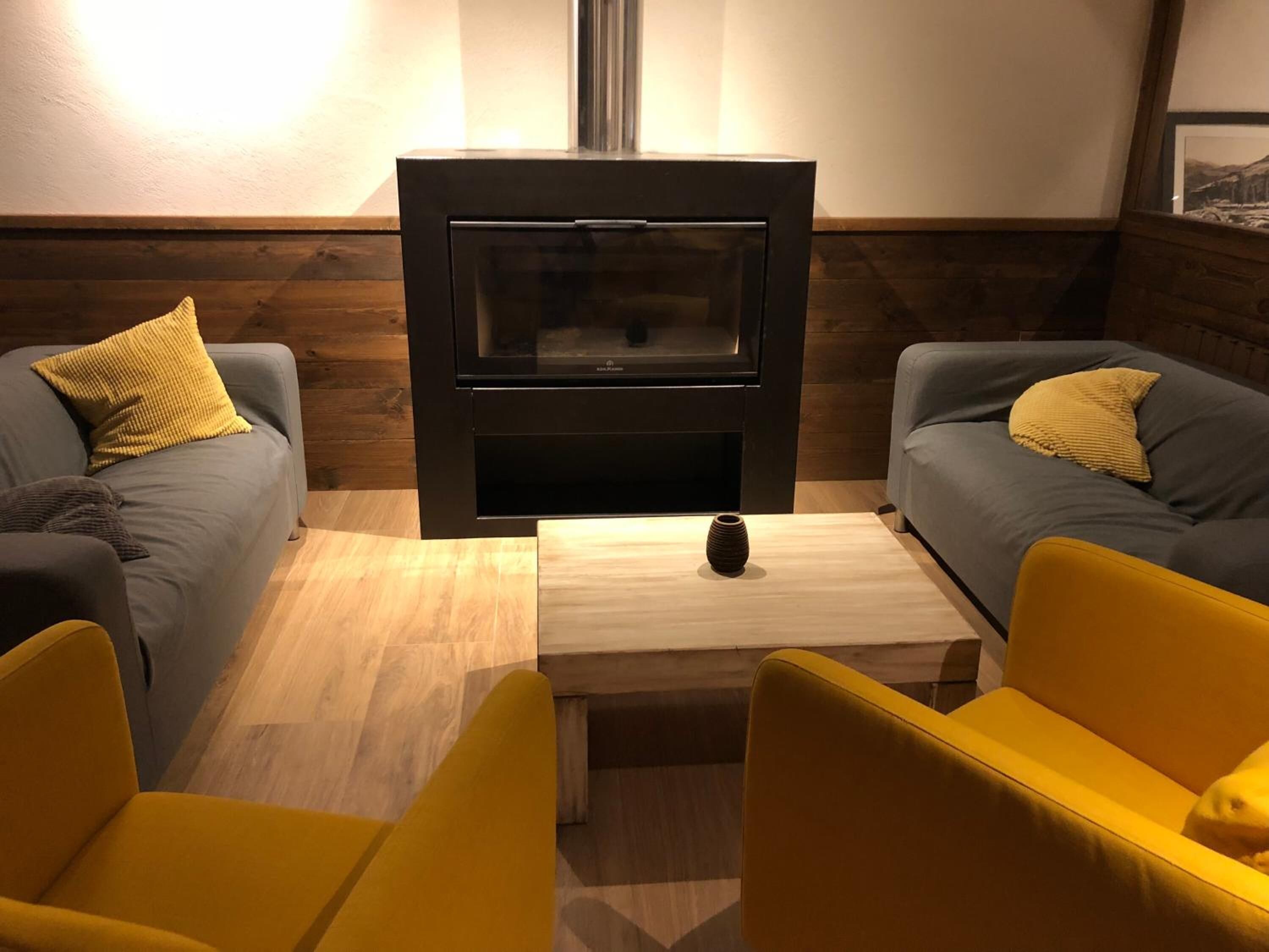 Ein gemütliches Wohnzimmer mit zwei grauen Sofas, einem Holztisch und einem schwarzen Kamin.