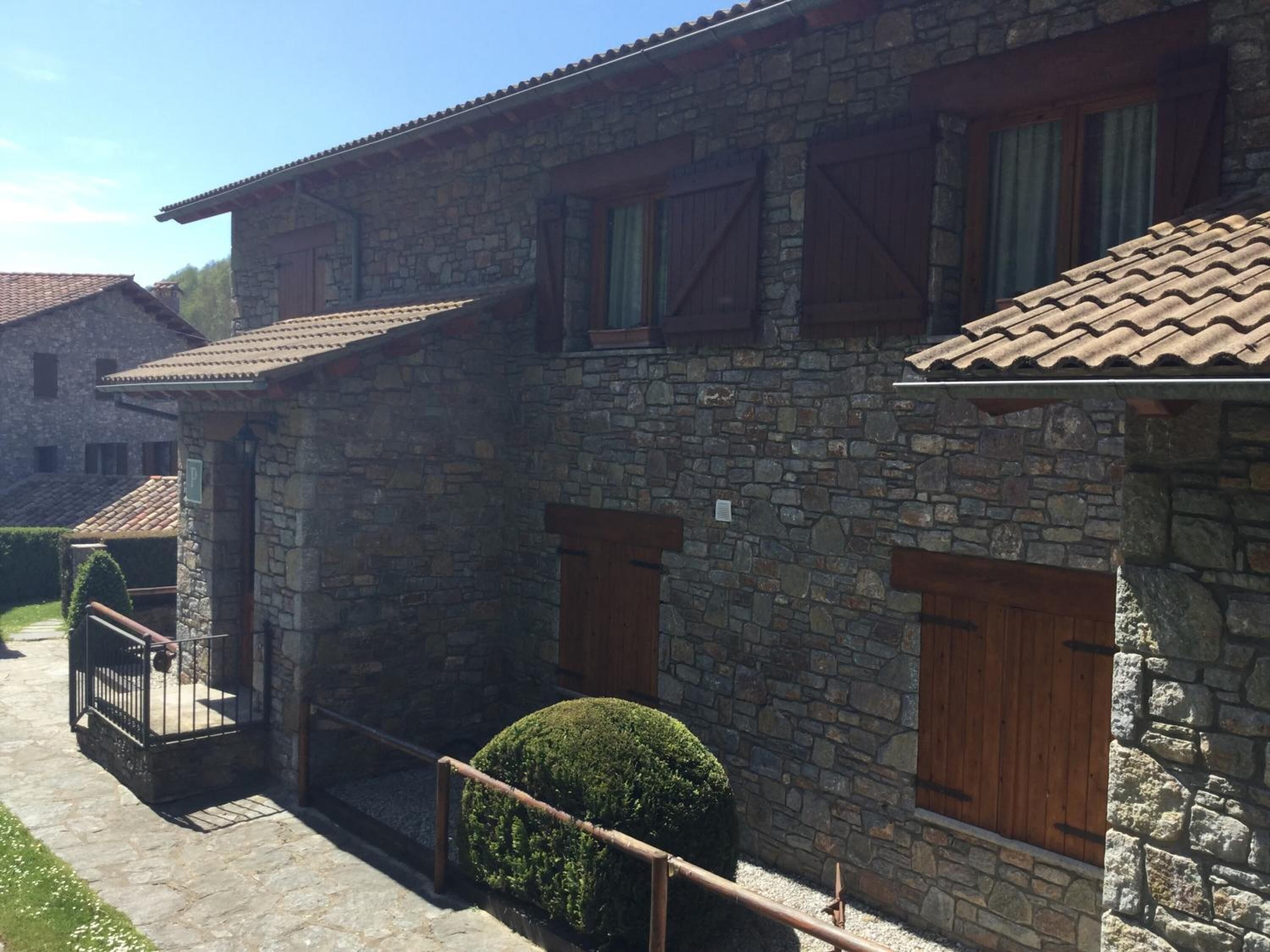 A stone building with a balcony, wooden shutters, and a small garden.