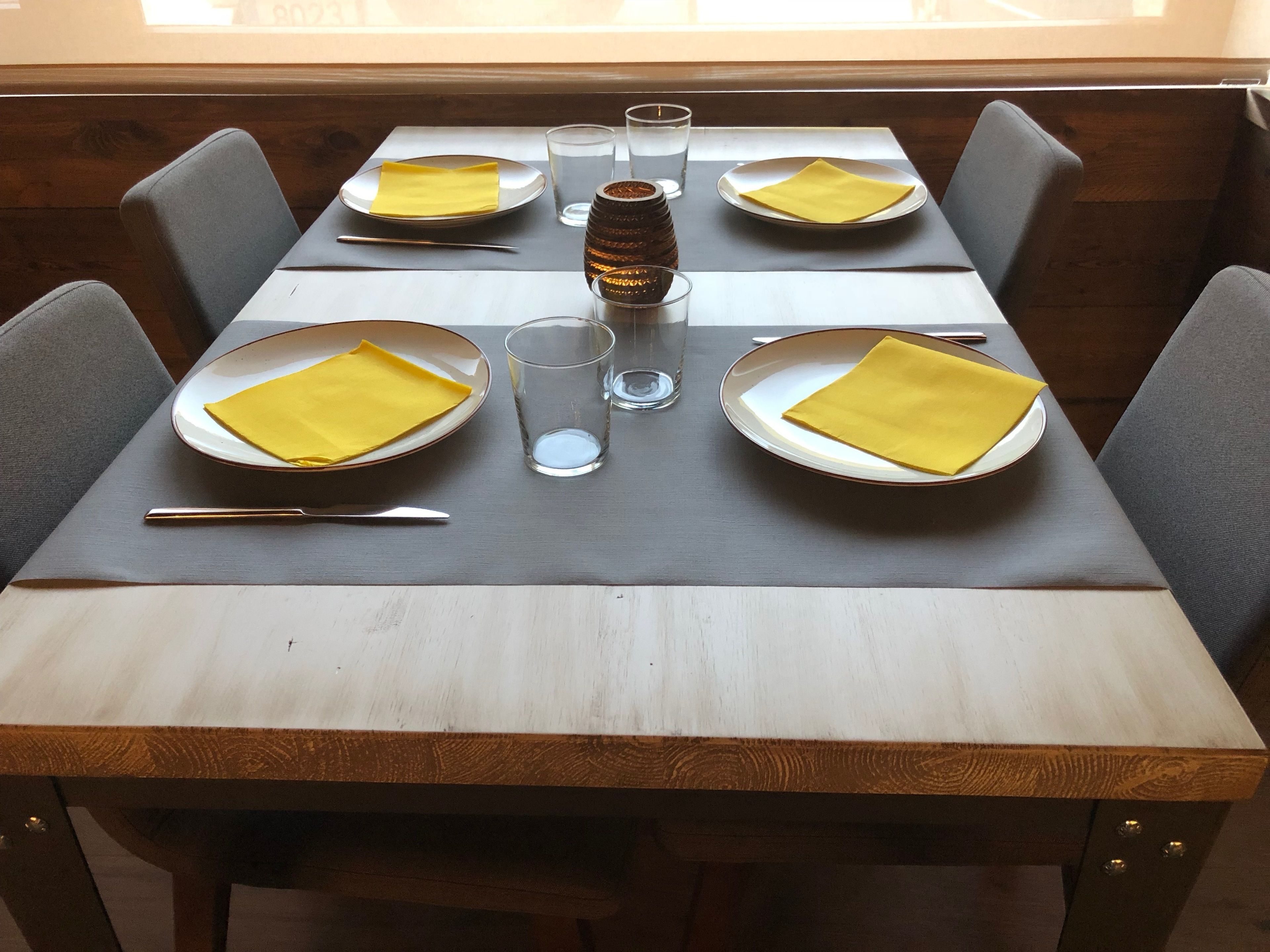 A dining table set with plates, napkins, cutlery, and glasses, with a wooden table and chairs.