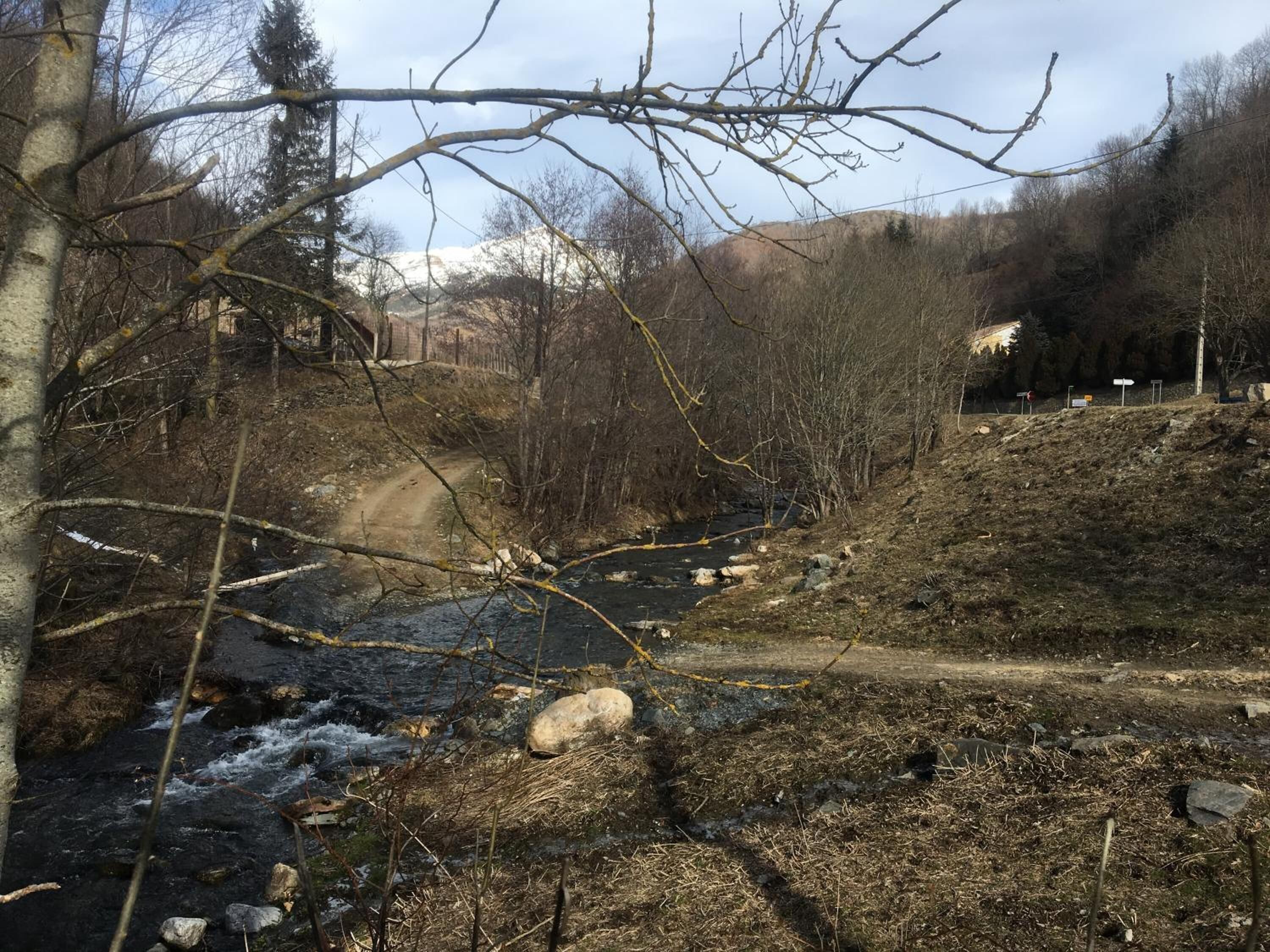 A natural landscape with a river, a dirt path, and trees.