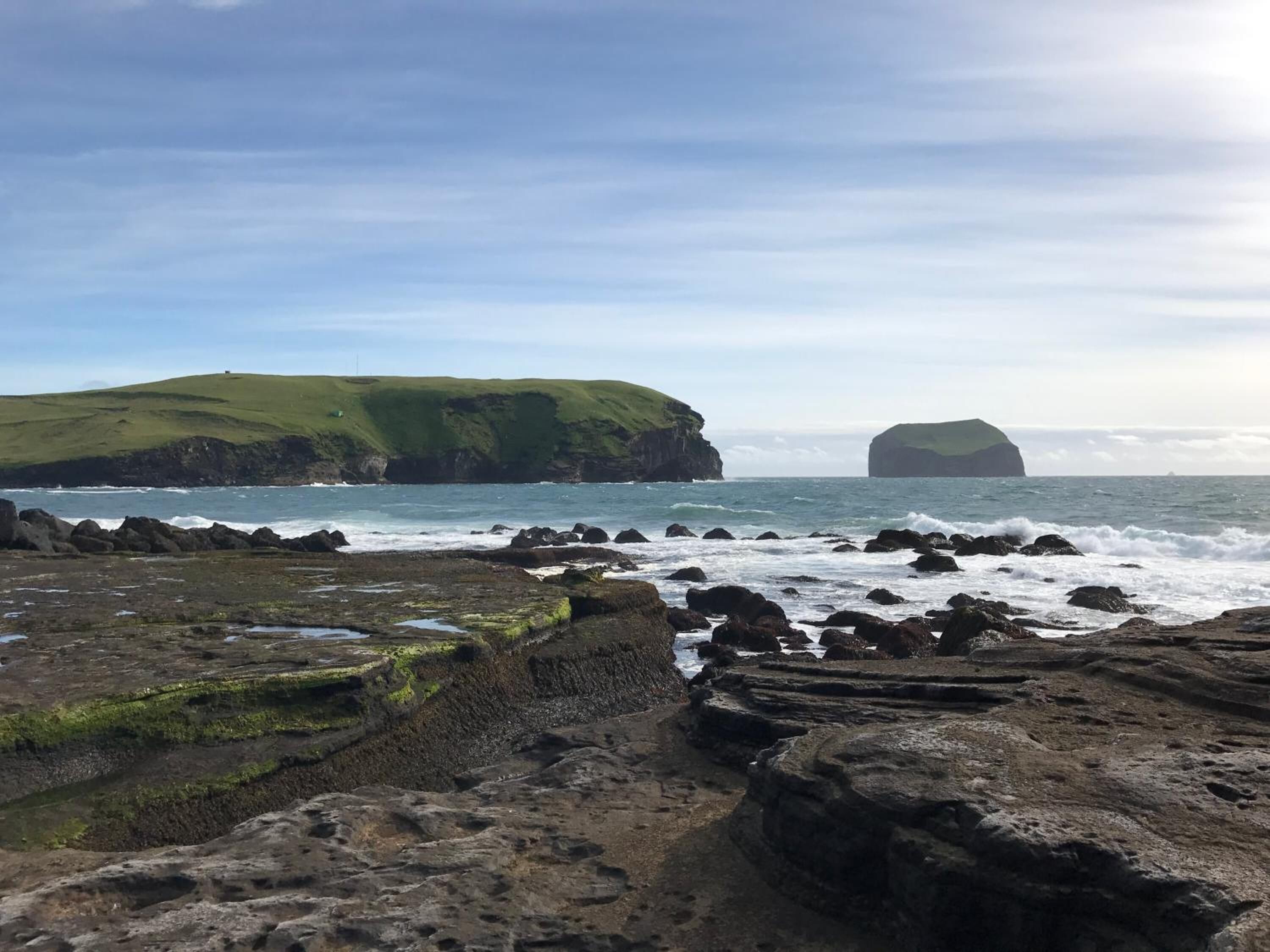 Un paysage côtier rocheux, avec une colline herbeuse et une île lointaine.