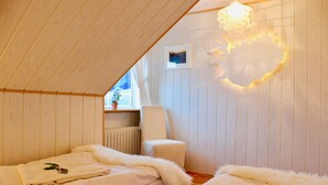 A cozy attic bedroom with two beds, a chair, and a decorative light fixture.