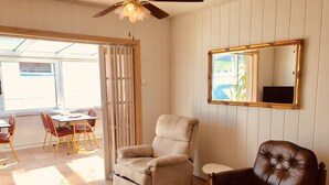 A room with a beige armchair, a brown leather chair, a ceiling fan, and a large mirror on the wall.