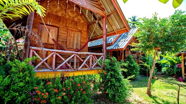 Una casa de madera con un porche, rodeada de vegetación exuberante y plantas florecientes.