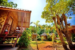 A rustic wooden building with a staircase leading to a porch, surrounded by lush greenery and other wooden structures.