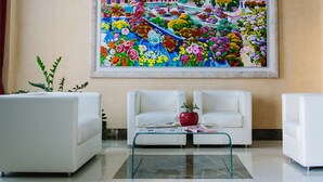 Een moderne lobby met witte banken, een glazen bijzettafeltje en een kleurrijk bloemen schilderij aan de muur.