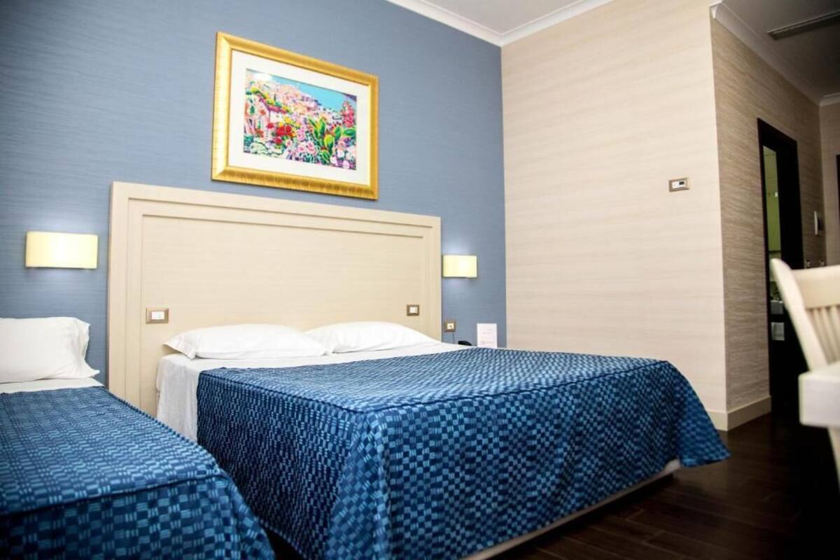 Een hotelkamer met twee bedden, een groot gepoft schilderij aan de muur en een stoel in de hoek.
