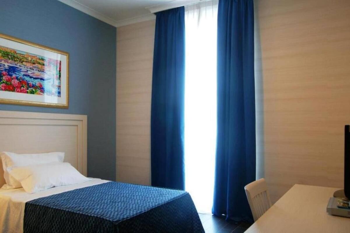 Hotelkamer met een bed, een bureau, een stoel, een schilderij aan de muur en een raam met blauwe gordijnen.