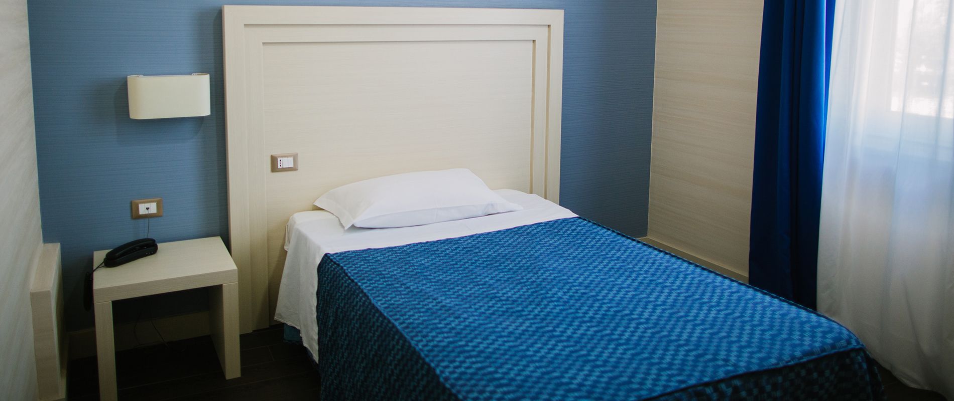 A single bed with a white headboard and a blue bedspread in a room with blue walls.