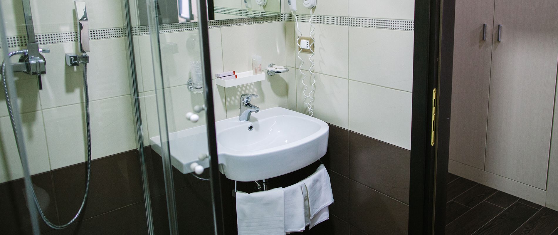 A bathroom with a glass shower enclosure, a white sink, and a towel rack.