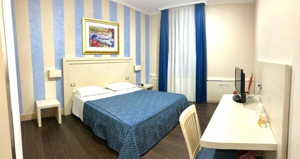 Una habitación de hotel con cama, escritorio, silla, televisor y un cuadro en la pared.