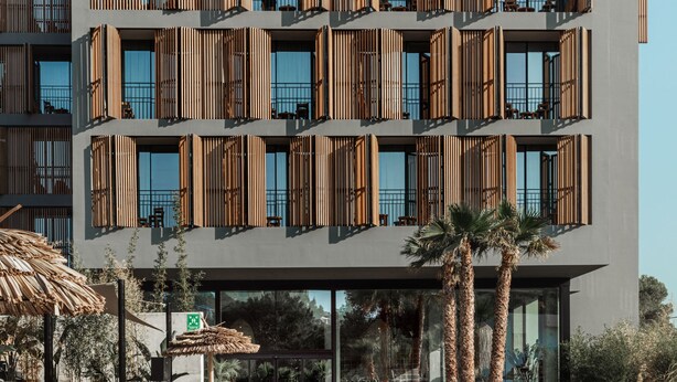 Un hotel moderno con piscina, terraza de madera y sillones de descanso.