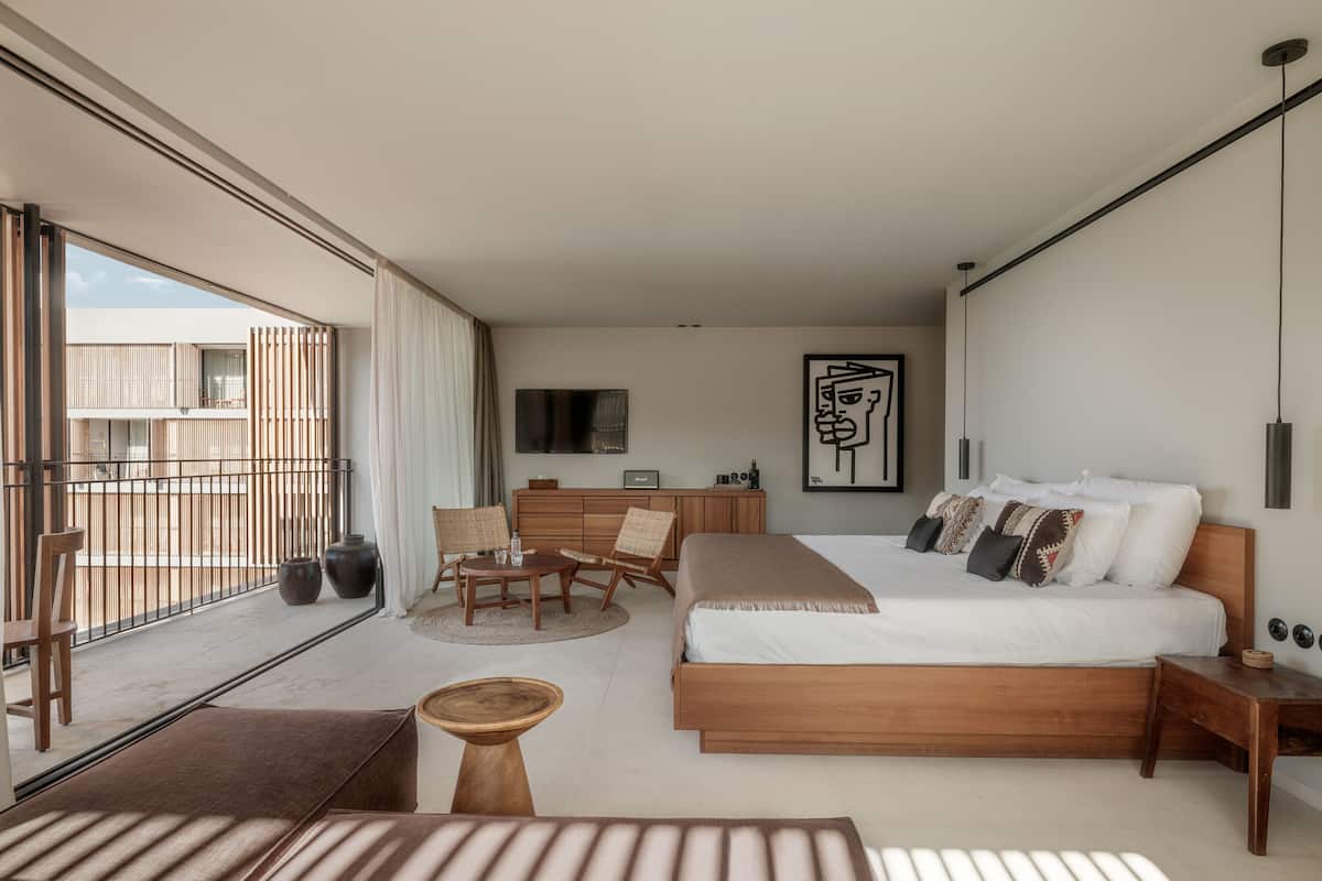 Habitación de hotel moderna con una cama grande, un escritorio, una silla, un televisor y un balcón con vistas a la ciudad.