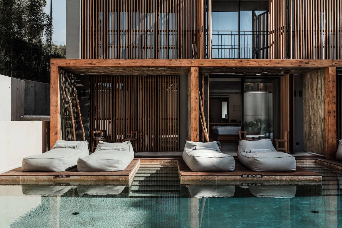 Zona de piscina exterior moderna con tumbonas de madera y vista a un edificio con listones verticales de madera.