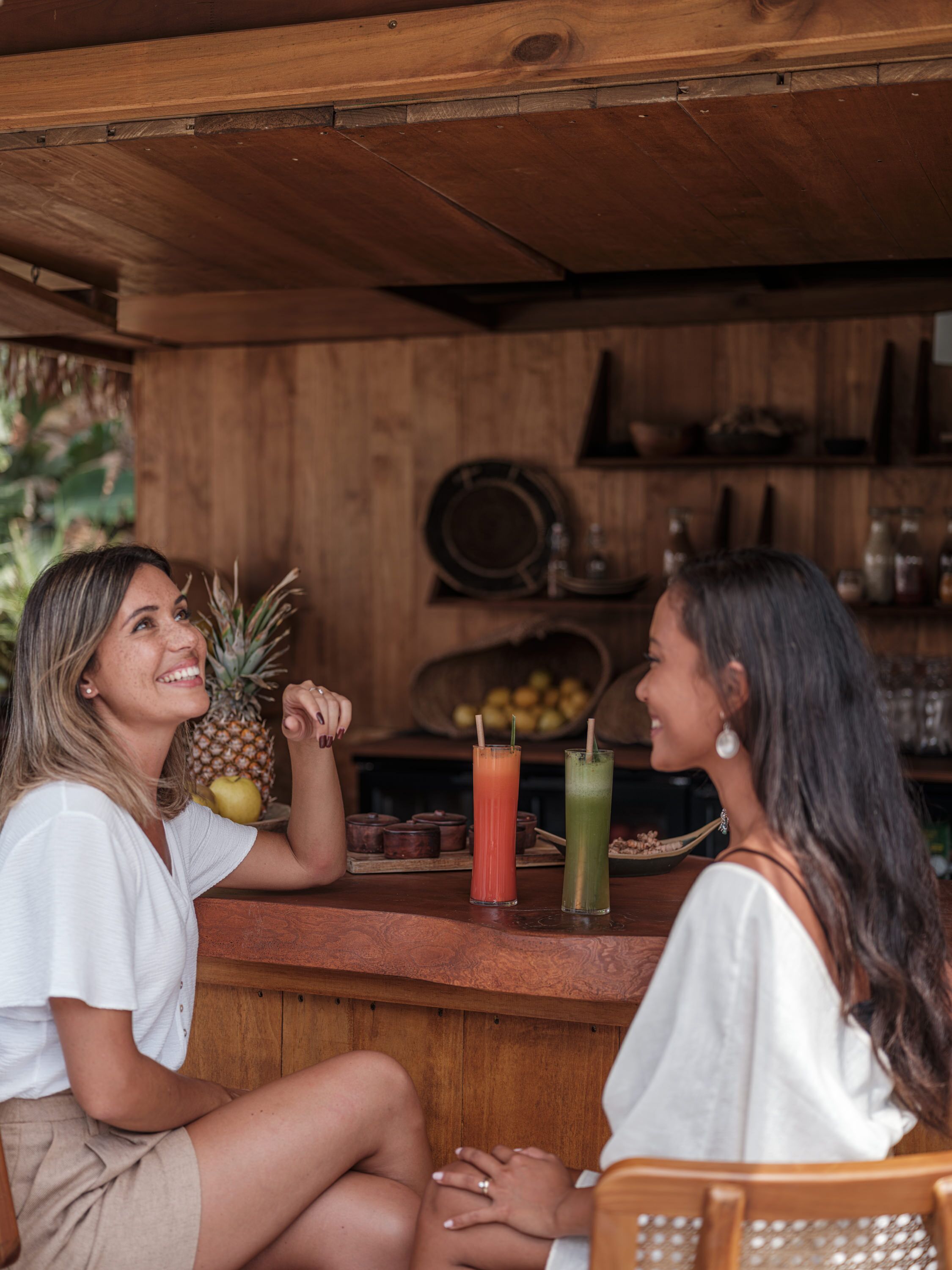 Dos personas sentadas en una barra de madera, con bebidas y una piña sobre la barra.