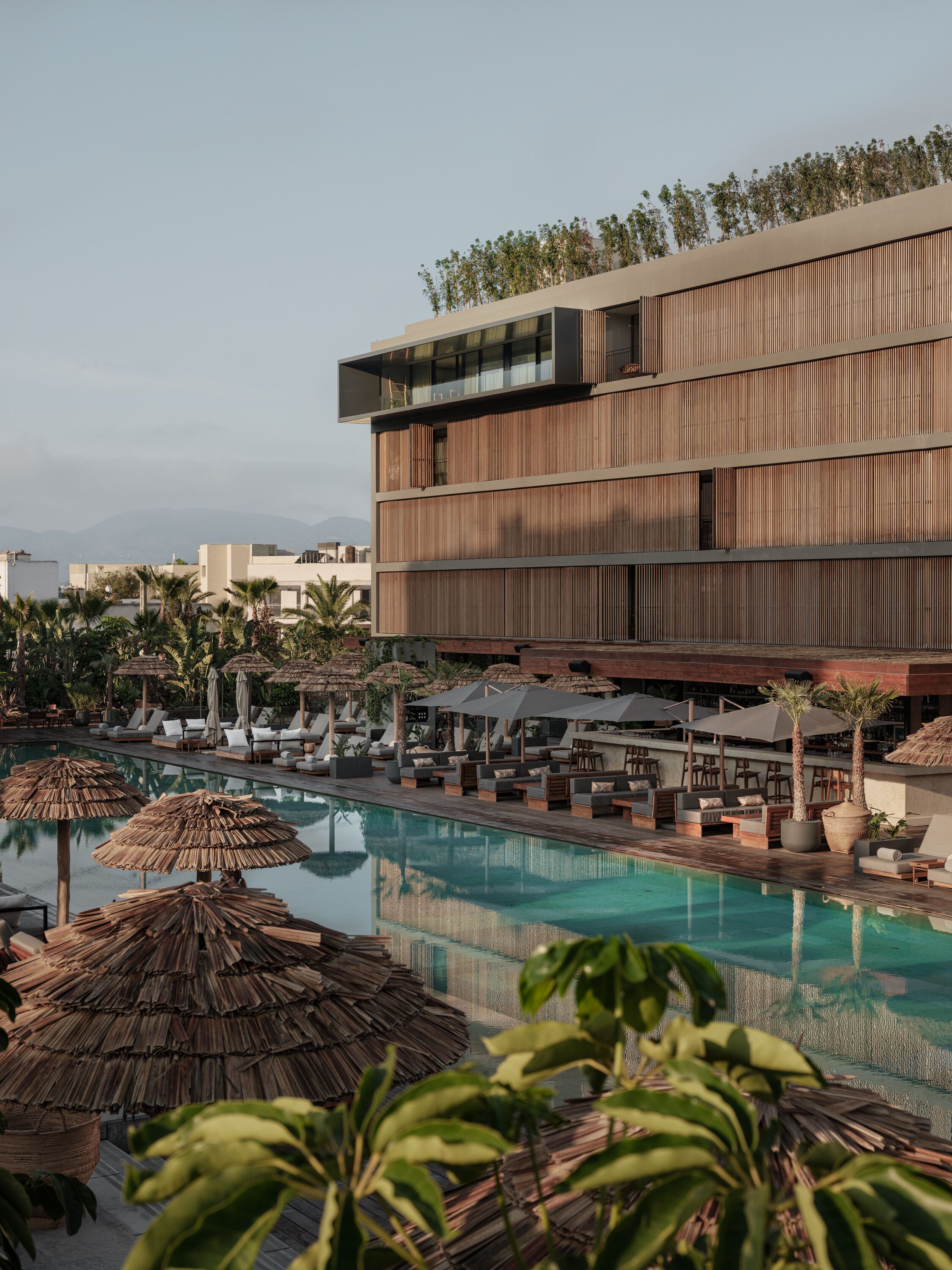 A modern hotel with a rooftop pool, lounge areas, and a view of the surrounding landscape.