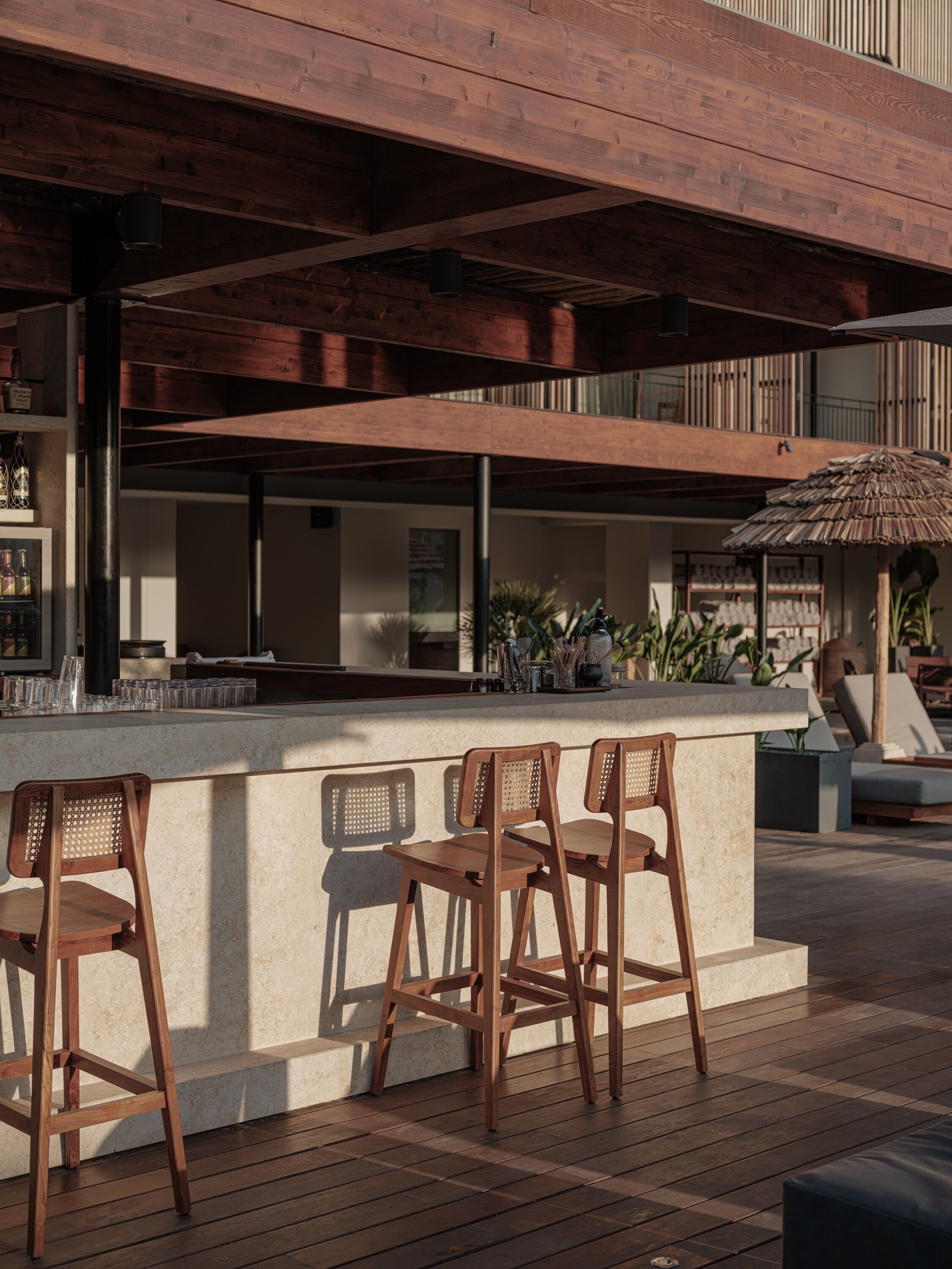 Een houten terras met een bar, barstoelen en een rieten parasol.