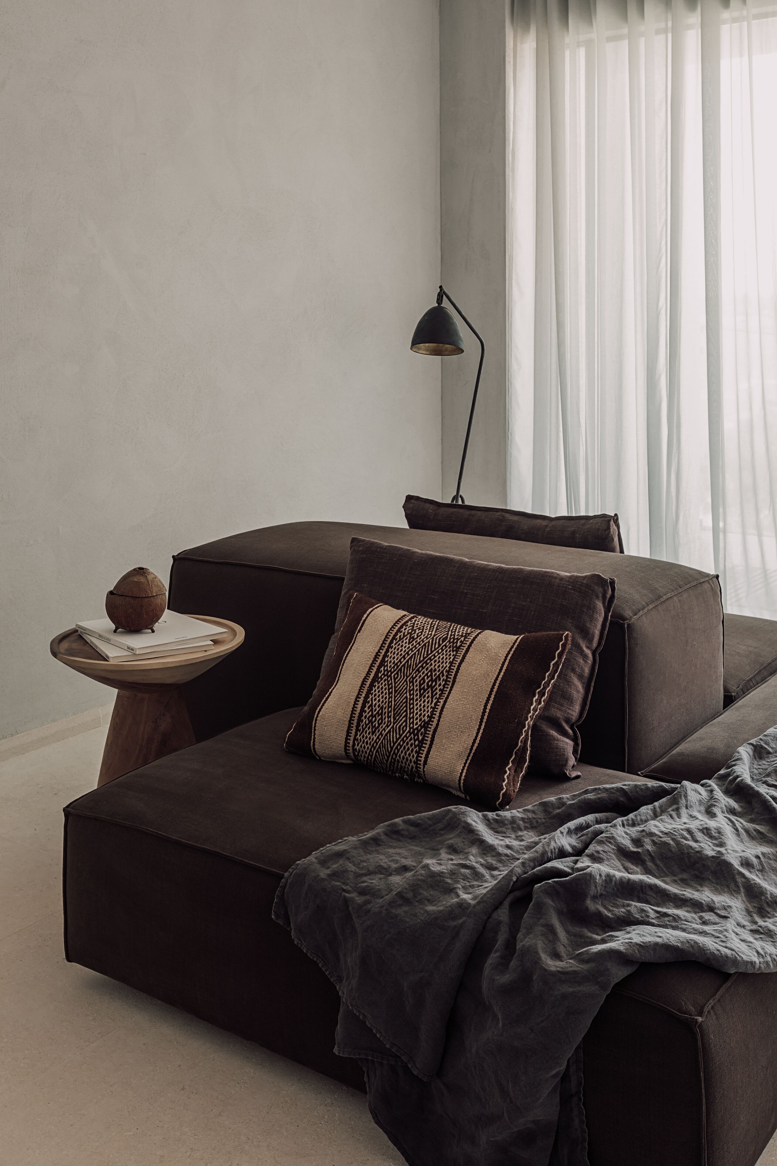 Un soggiorno moderno con un divano scuro, un tavolino con un libro e un oggetto decorativo, e una lampada da terra.
