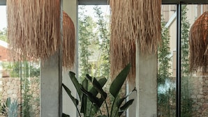 Una sala de estar moderna con un amplio sofá modular, lámparas colgantes de fibras tejidas y grandes ventanales que ofrecen vistas a la vegetación y una pared de piedra.