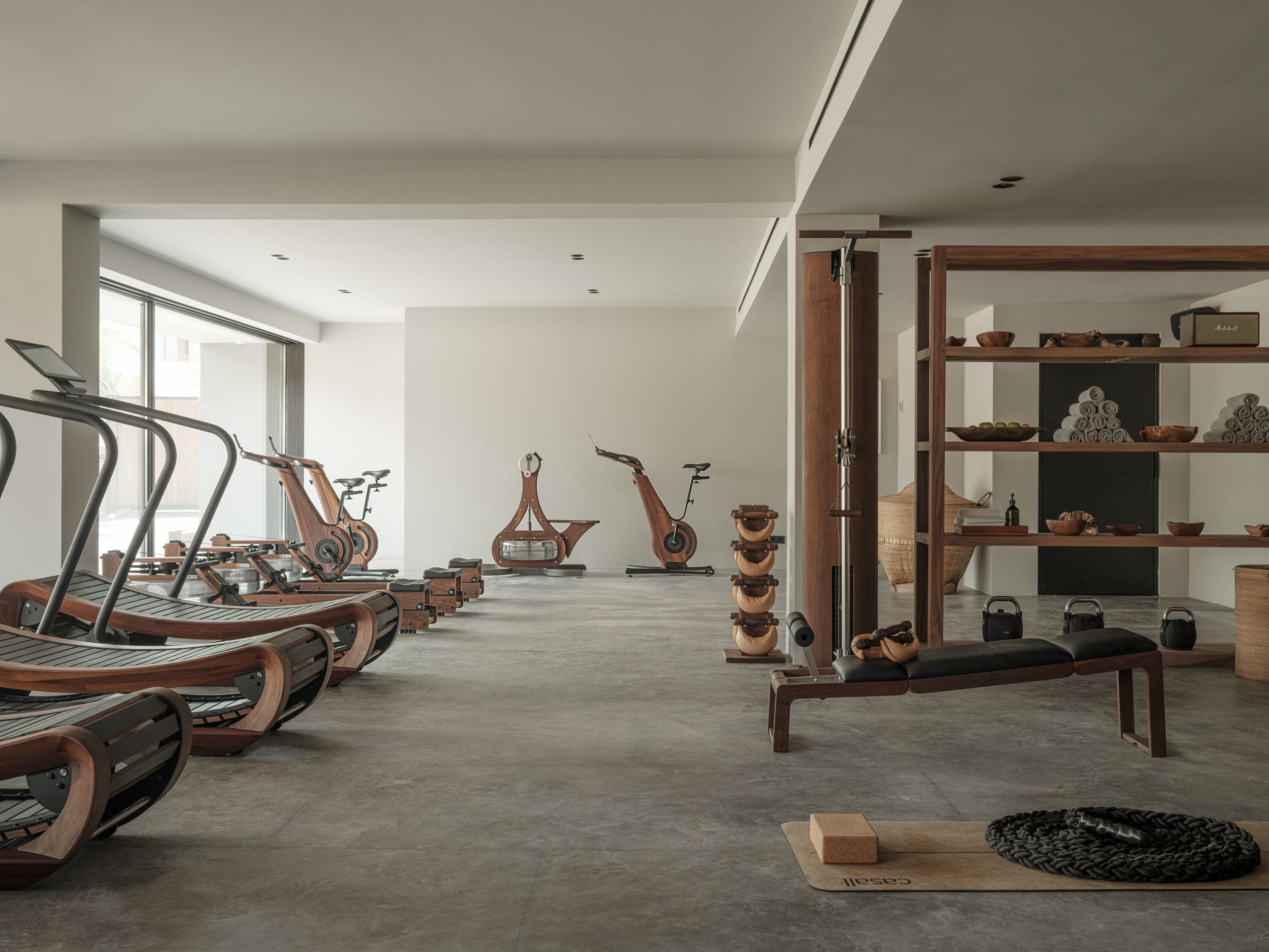 A spacious room with a long row of wooden exercise bikes, a large window, and a wooden shelf with various items.