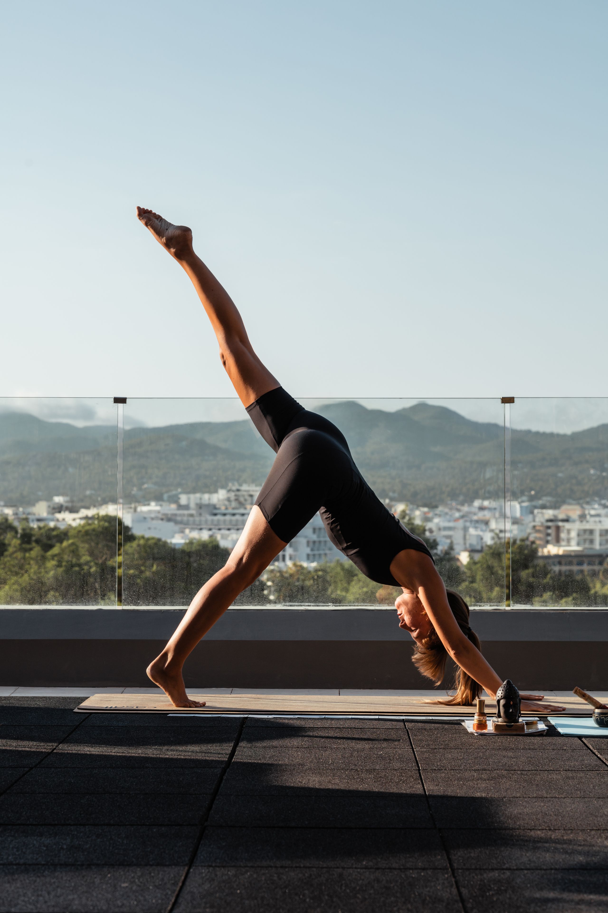 A person performing a yoga pose on a rooftop with a cityscape and mountains in the background.
