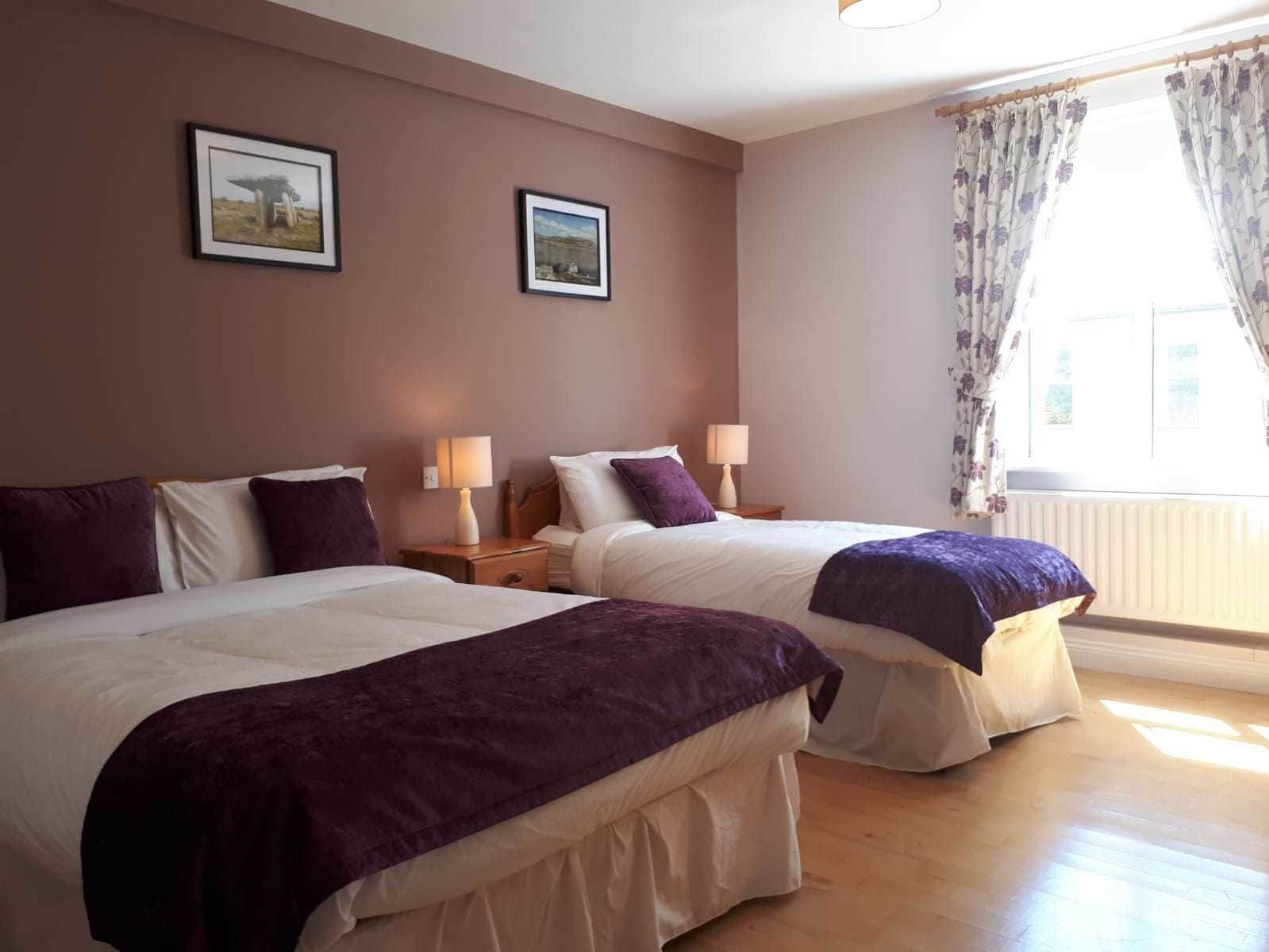 A hotel room with two beds, a window with curtains, and two framed pictures on the wall.