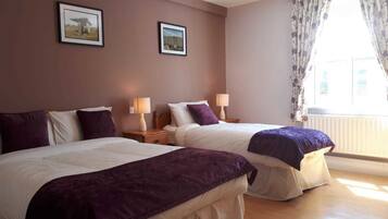 A hotel room with two beds, a window with curtains, and two framed pictures on the wall.