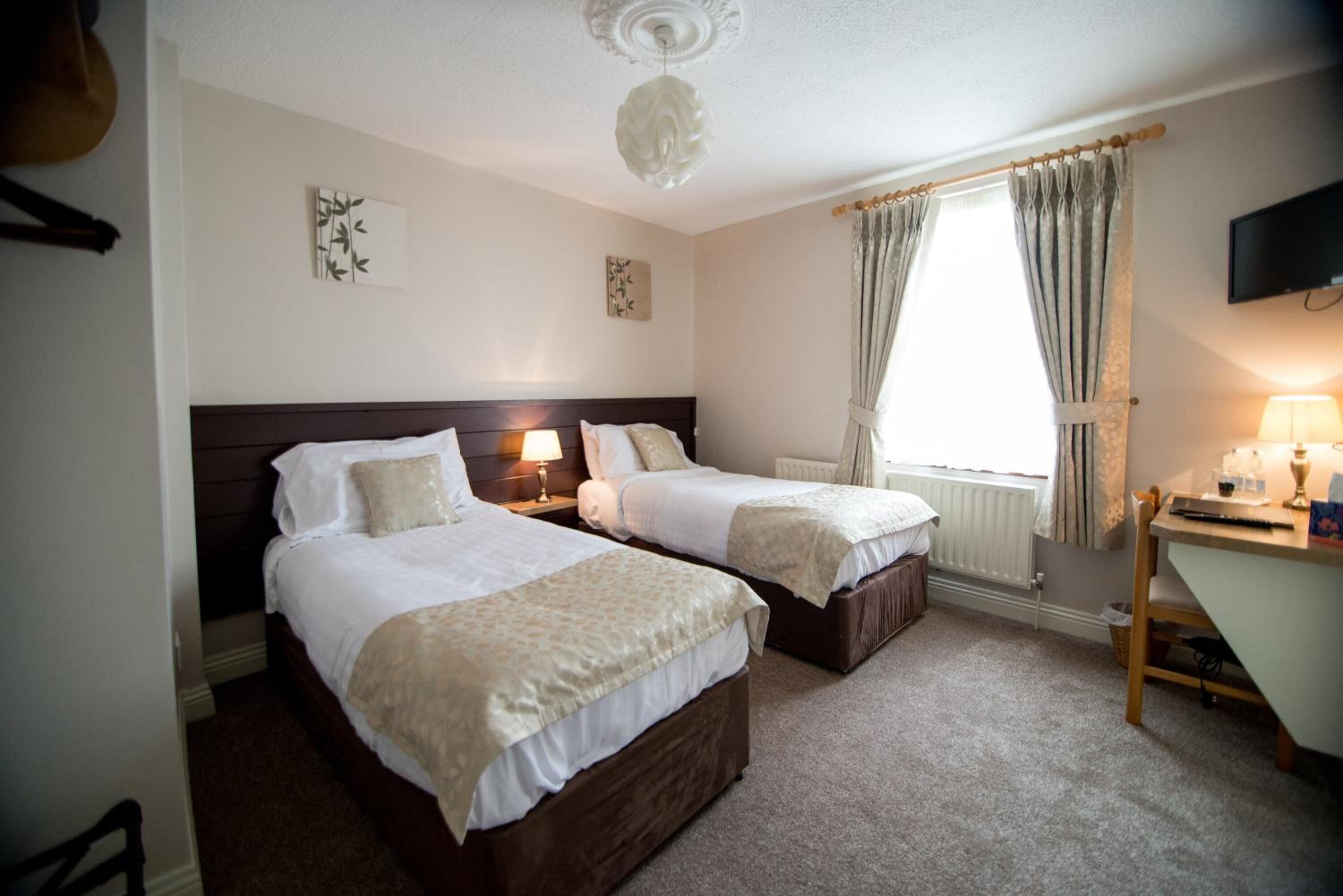 A hotel room with two beds, a desk, a chair, and a television.