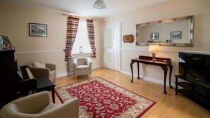 A living room with a piano, a red patterned rug, a television, and a mirror on the wall. - The Ritz House (Lisdoonvarna)