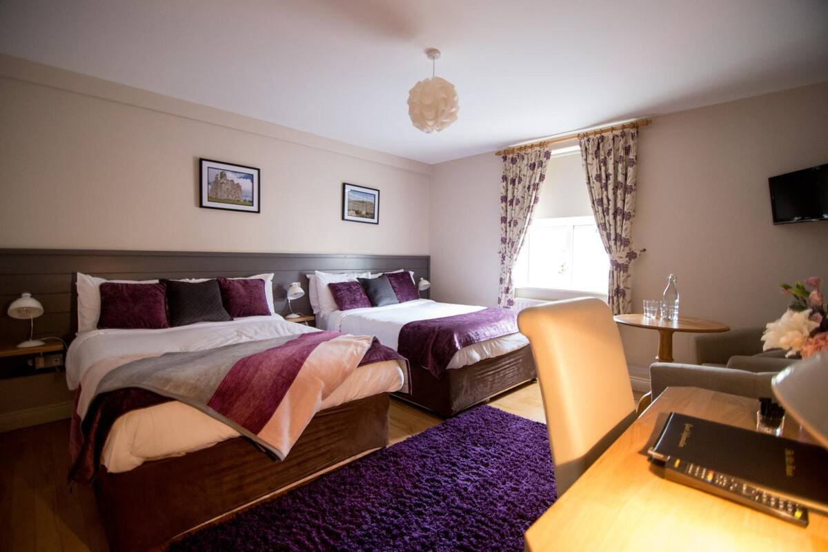 Ein Hotelzimmer mit zwei Betten, einem Schreibtisch, einem Stuhl, einem Fernseher und einem Fenster mit Vorhängen.