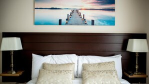 A hotel room with a bed, two bedside lamps, a nightstand, and a wall-mounted painting of a sunset over a pier. - The Ritz House (Lisdoonvarna)