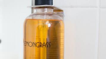Dispensador de jabón líquido con bomba, etiquetado como “LEMONGRASS CLEANSING HAND WASH”, montado en una pared de azulejos blancos.