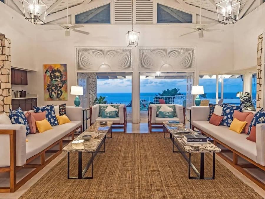 A spacious living area with a view of the ocean, furnished with sofas and coffee tables, and a stone accent wall.