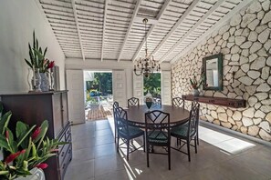 Un comedor con una mesa redonda, sillas, una araña y una pared de piedra con un espejo.