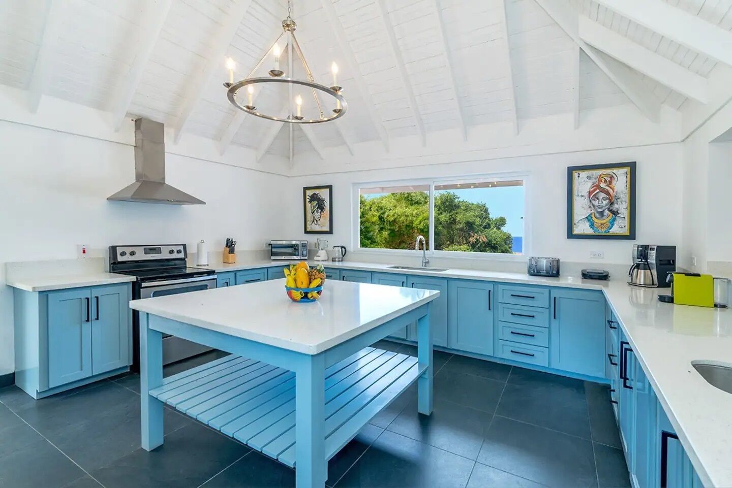 Cocina moderna con armarios azules, una isla blanca y un ventanal con vistas a zonas verdes.