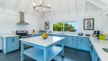 Cocina moderna con armarios azules, una isla blanca y un ventanal con vistas a zonas verdes.
