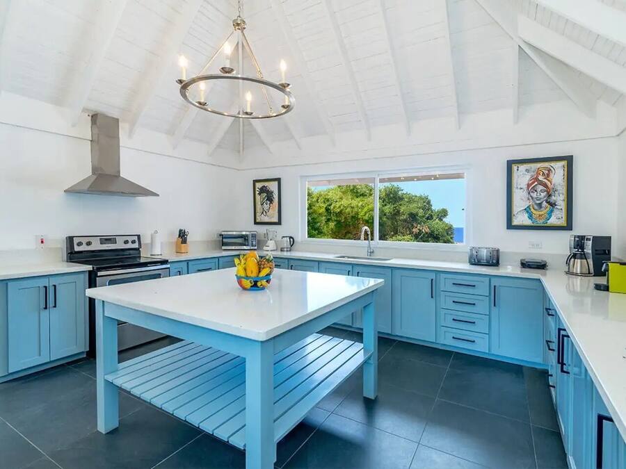 Cocina moderna con armarios azules, una isla blanca y un ventanal con vistas a zonas verdes.