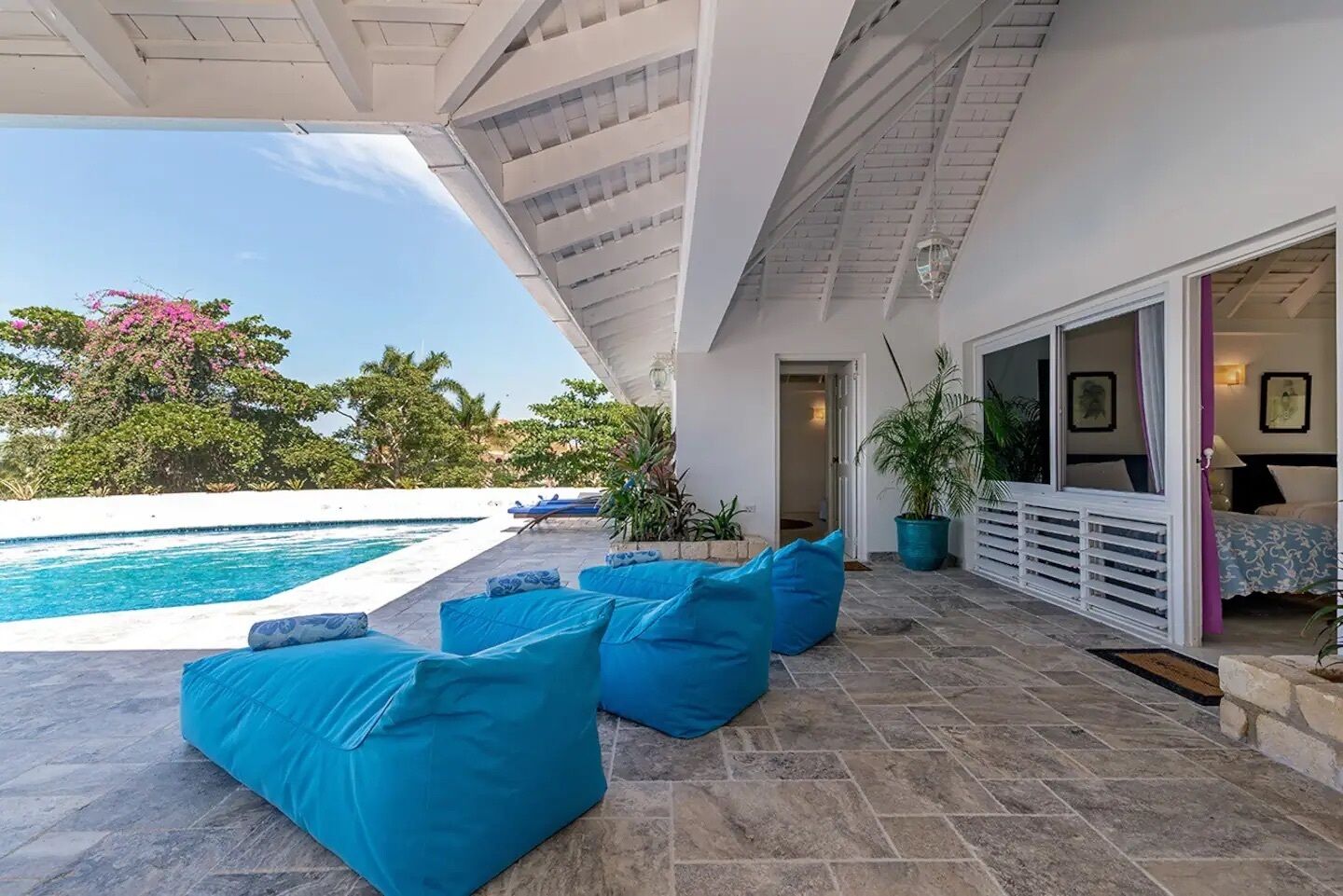 A poolside area with blue cushioned seating, a swimming pool, and a view of the surrounding greenery.