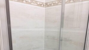 A glass-enclosed shower stall with a tiled floor and a decorative border at the top. - White house Hotel (London)