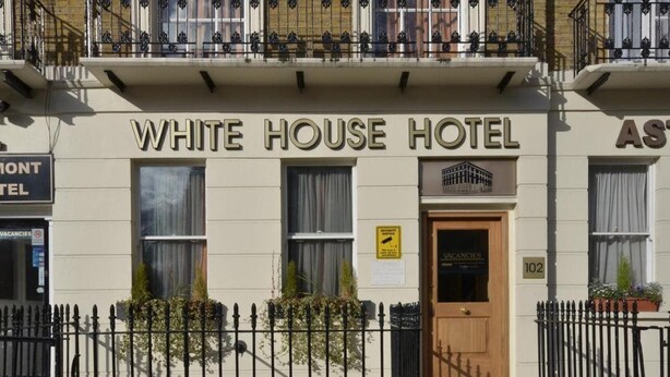 The exterior of the White House Hotel with a wooden door, a sign indicating vacancies, and a number '102' on the wall. - White house Hotel (London)
